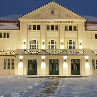 Beleuchtete Fassade des Lessingtheater-Gebudes im Winter. Auf dem Vorplatz liegt Schnee.