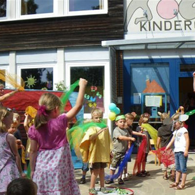 Eingangsbereich des Kindergartens Ahlum: Kinder tanzen mit bunten Tüchern vor dem Gebäude des Kindergartens.
