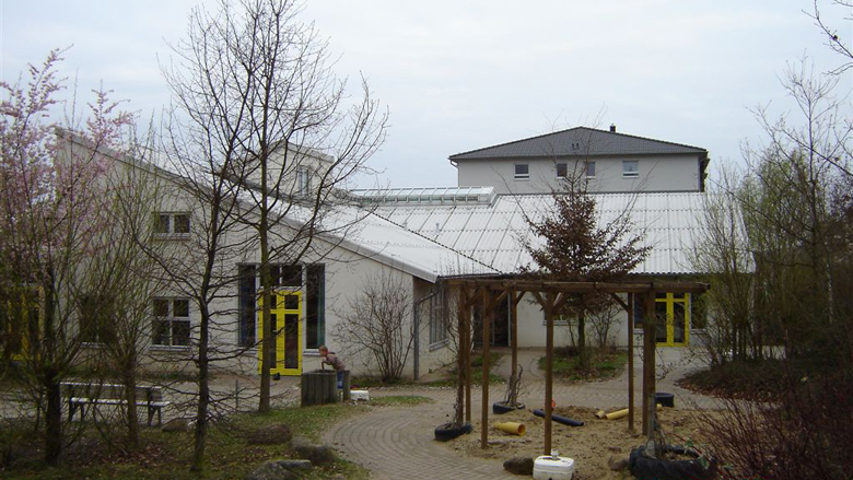 Außenanlage und Gebäude des Kindergartens Martin Luther. Sand- und Rasenflächen.