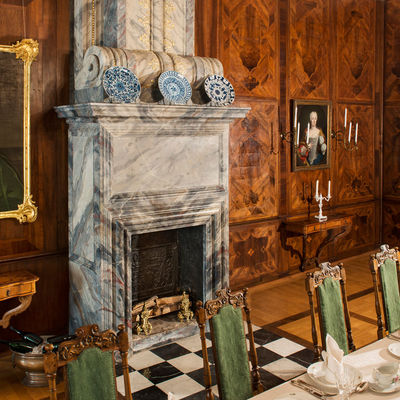 Das Foto zeigt einen Blick in die Ausstellung. In einem Raum mit Holzvertäfelung und Kamin steht eine reich gedeckte Festtafel. An den Wänden hängen Kerzen und Gemälde der herzoglichen Familie.