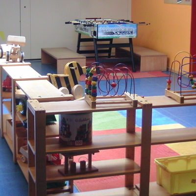Spielecke mit buntem Fußboden, Holzregalen mit Spielzeug und einem Tischkicker