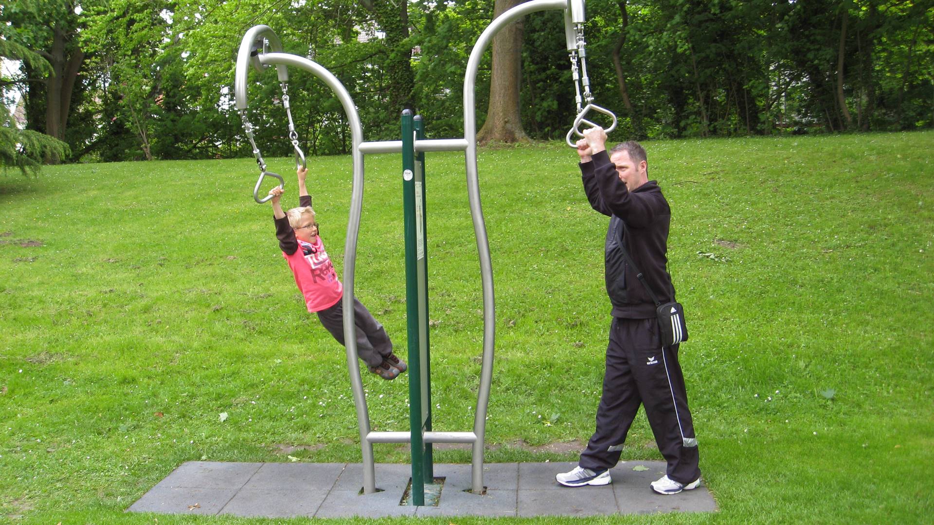 Ein Mann und ein Kind trainieren an einer Station im Park.