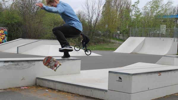 Ein Junge fliegt mit seinem Skateboard in der Luft über ein Skateelement aus Beton