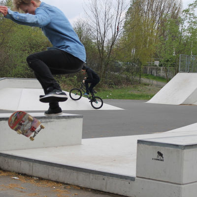Ein Junge fliegt mit seinem Skateboard in der Luft über ein Skateelement aus Beton