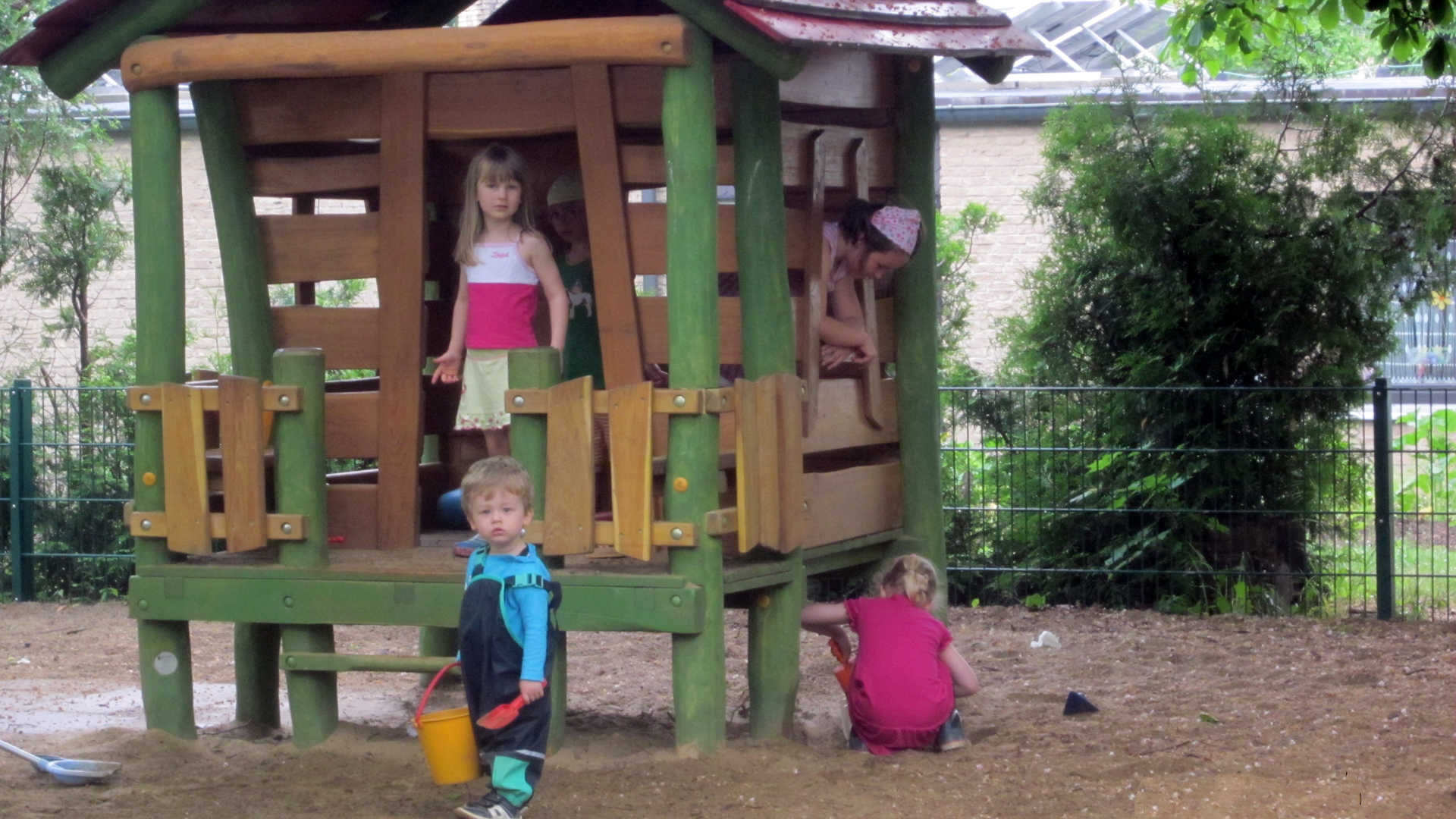 Außengelände des Kindergartens St. Ansgar zu sehen. Vier Kinder spielen gern in dem kleinen, bunten Gartenhäuschen aus Holz