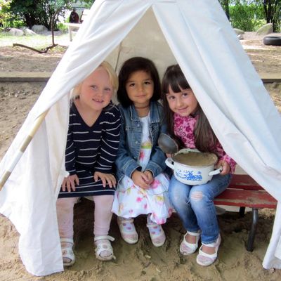 Drei Mädchen sitzen in einem Zelt mitten in der Sandkiste.