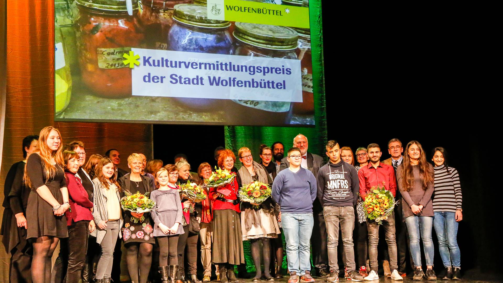 Gruppenbild, im Hintergrund ein großes Plakat mit der Aufschrift "Kulturvermittlungspreis der Stadt Wolfenbüttel".