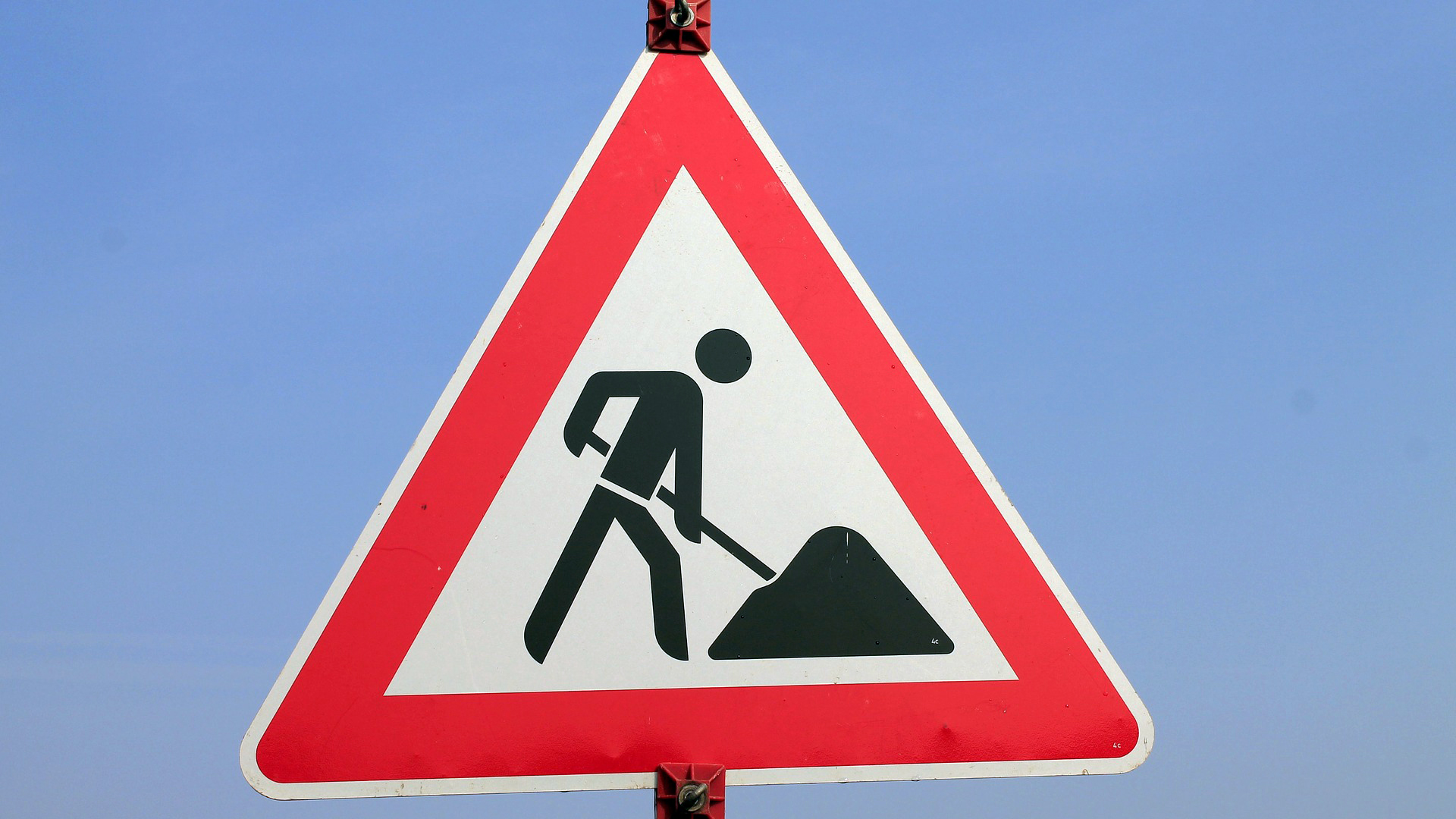 Das Verkehrsschild "Achtung Bauarbeiten". Ein weißes Dreieck mit rotem Rand, mittig ein Männchen mit einer Schaufel.