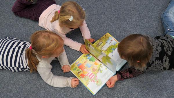 Drei Kinder liegen auf dem Fußboden und schauen sich ein Bilderbuch an.