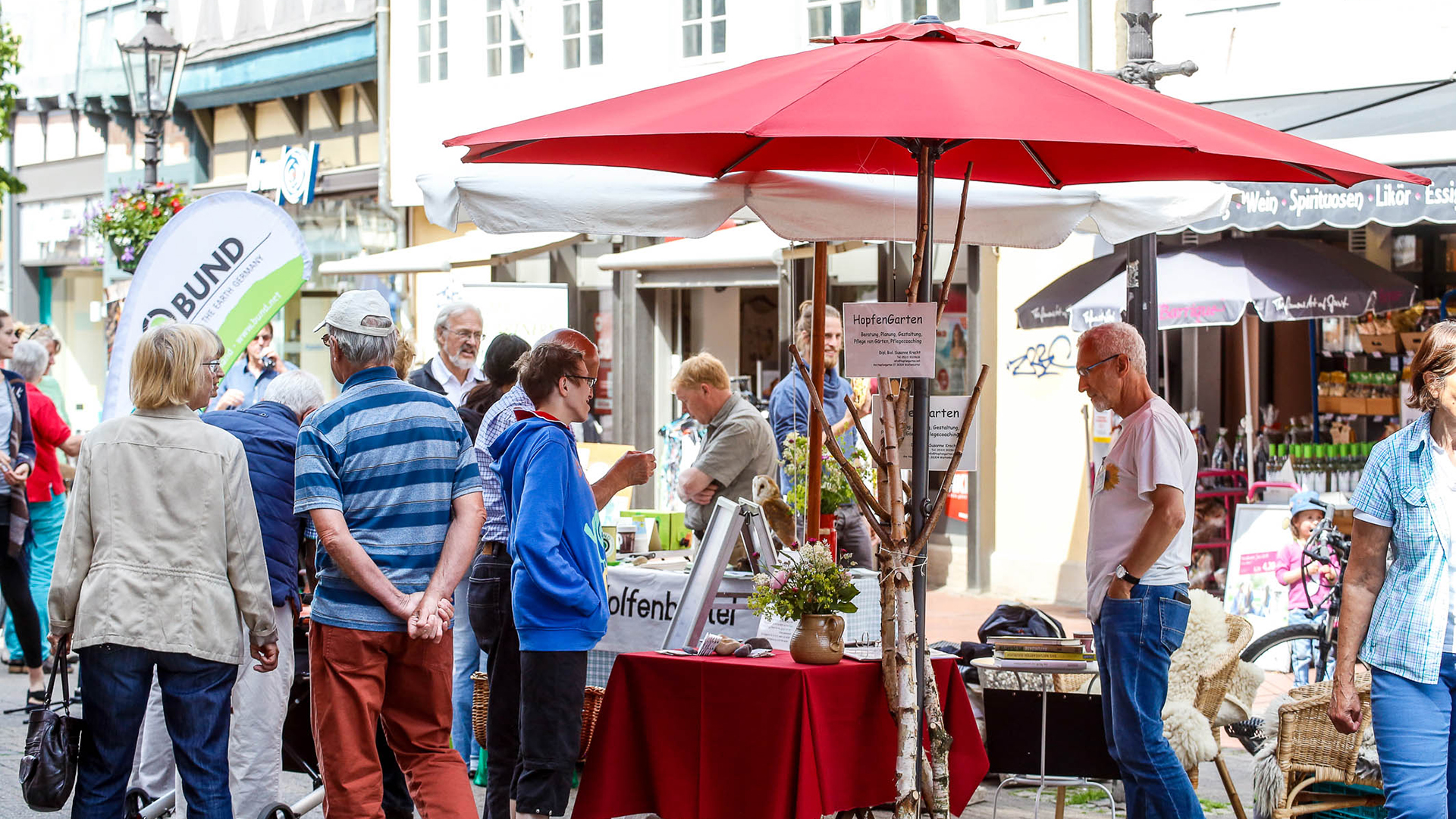 Ein Stand mit einem roten Schirm in der Innenstadt von Wolfenbüttel. An dem Menschen sich informieren.