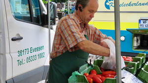 Hinter einem Marktstand steht ein Mann und packt eine Tüte mit Gemüse.
