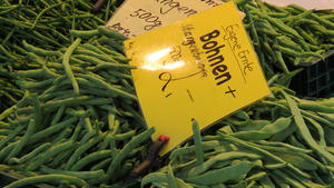 Bild von Kisten mit Bohnen. Auf einem gelben Schild werden die Bohnen aus eigener Ernte mit 2 Euro je 500 Gramm beworben.