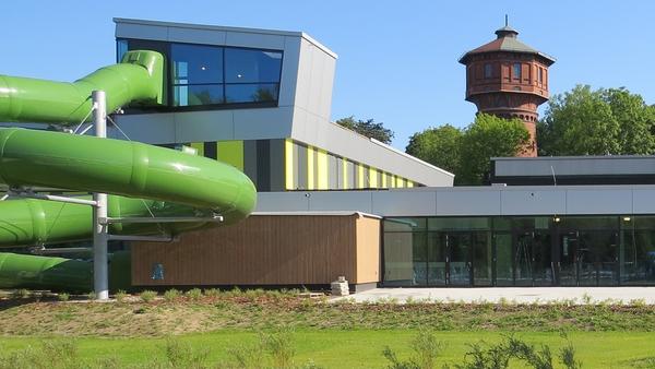 Gebäude des Stadtbads Okeraue in Wolfenbüttel mit grüner Wasserrutsche. Im Hintergrund ist der Wasserturm zu erkennen.
