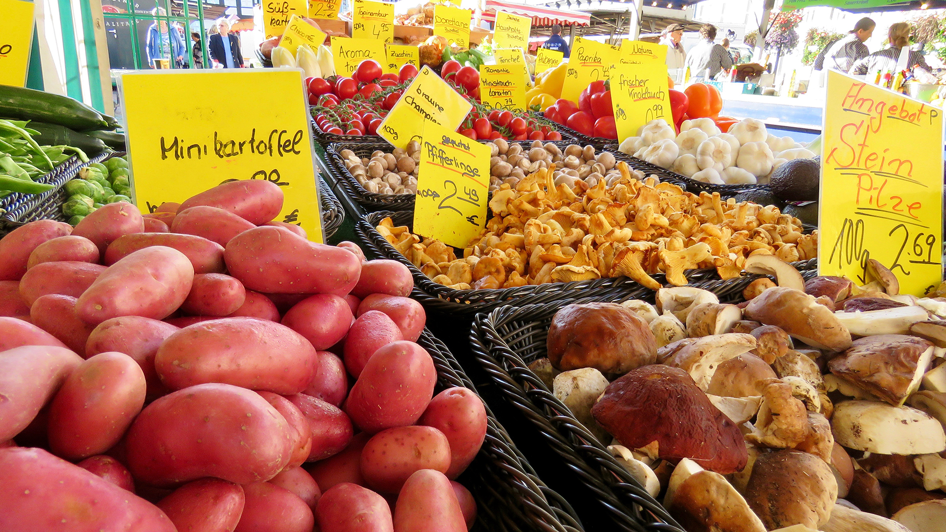 In Auslagen an einem Marktstand werden unter anderem Minikartoffeln und verschiedene Pilzsorten angeboten.