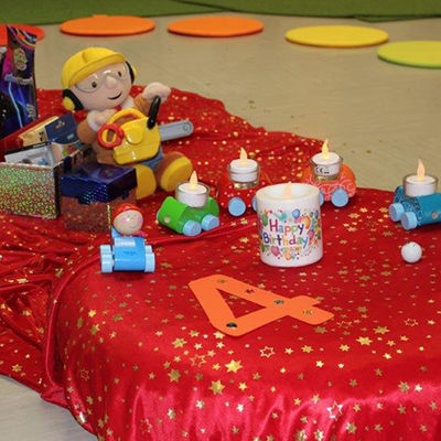 In einer Mitte eines Sitzkreises sind Spielzeuge und die Nummer Vier aus Pappe aus Kissen platziert.