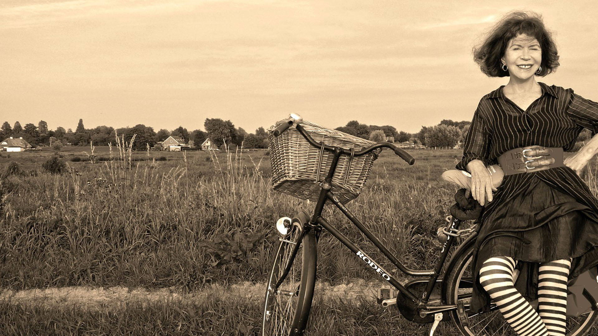 An einem Feldrand lehnt sich eine Frau an ein abgestelltes Fahrrad.