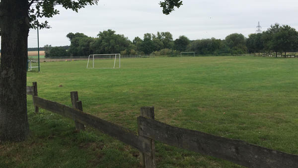 Auf einer grünen Wiese steht ein Fußballtor ohne Tornetz. Im Vordergrund ist ein Holzzaun zu erkennen.