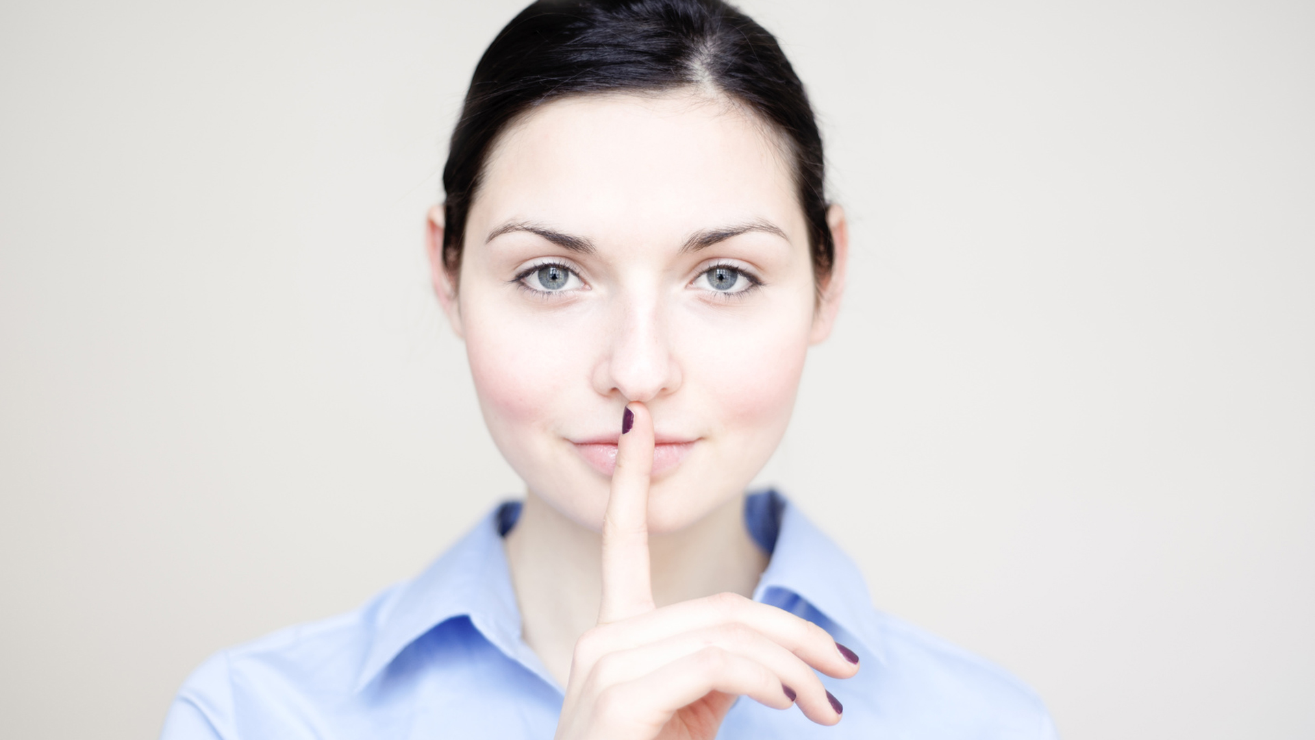 Eine Frau hält sich den Zeigefinger vor den geschlossenen Mund/die Lippen.
