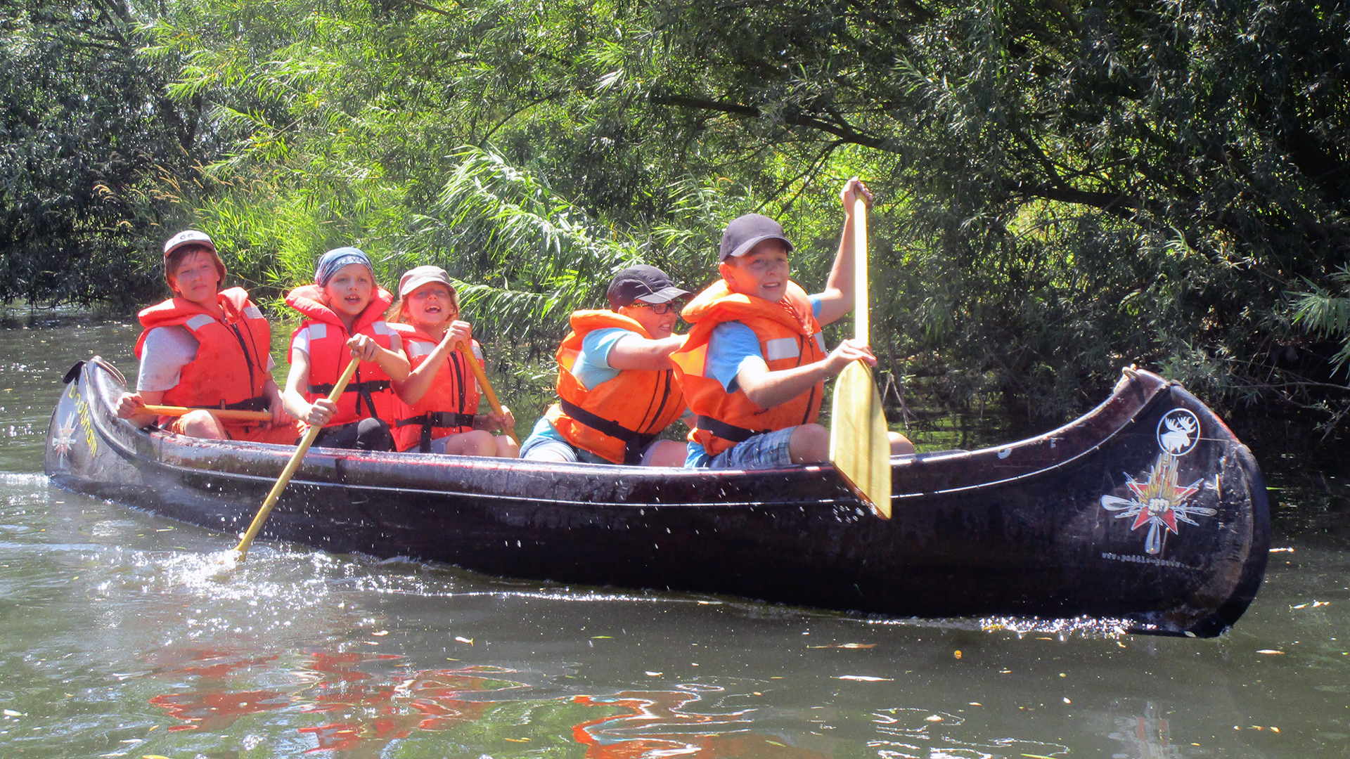 Kinder paddeln in einem Kanu auf einem Fluss.