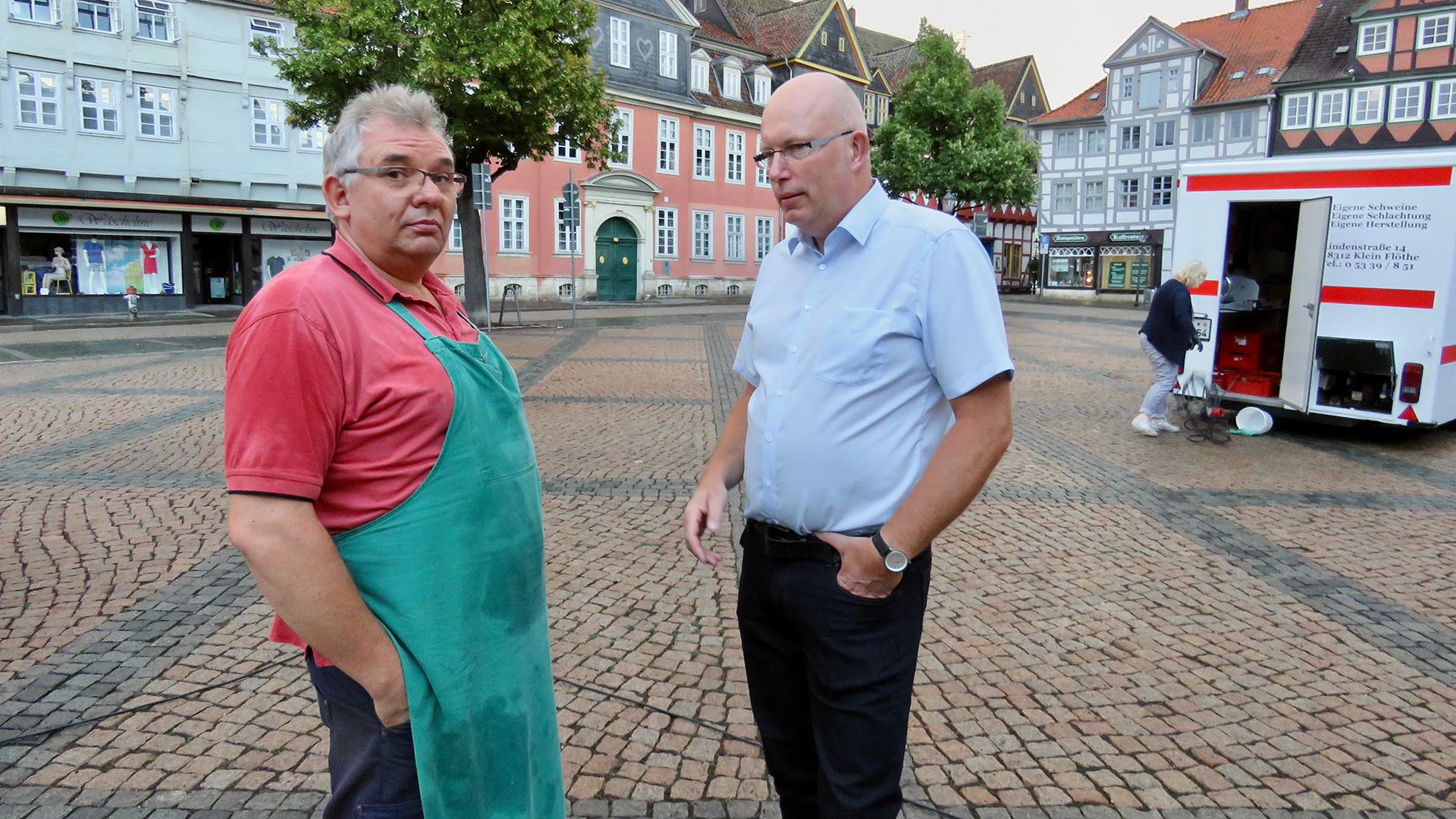 Zwei Männer stehen auf dem Marktplatz in Wolfenbüttel. Der Mann links im Bild trägt eine grüne Schürze.