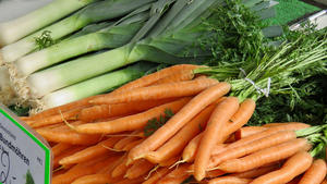 Auf einem Marktstand liegen mehrere Karotten und Lauchstangen.