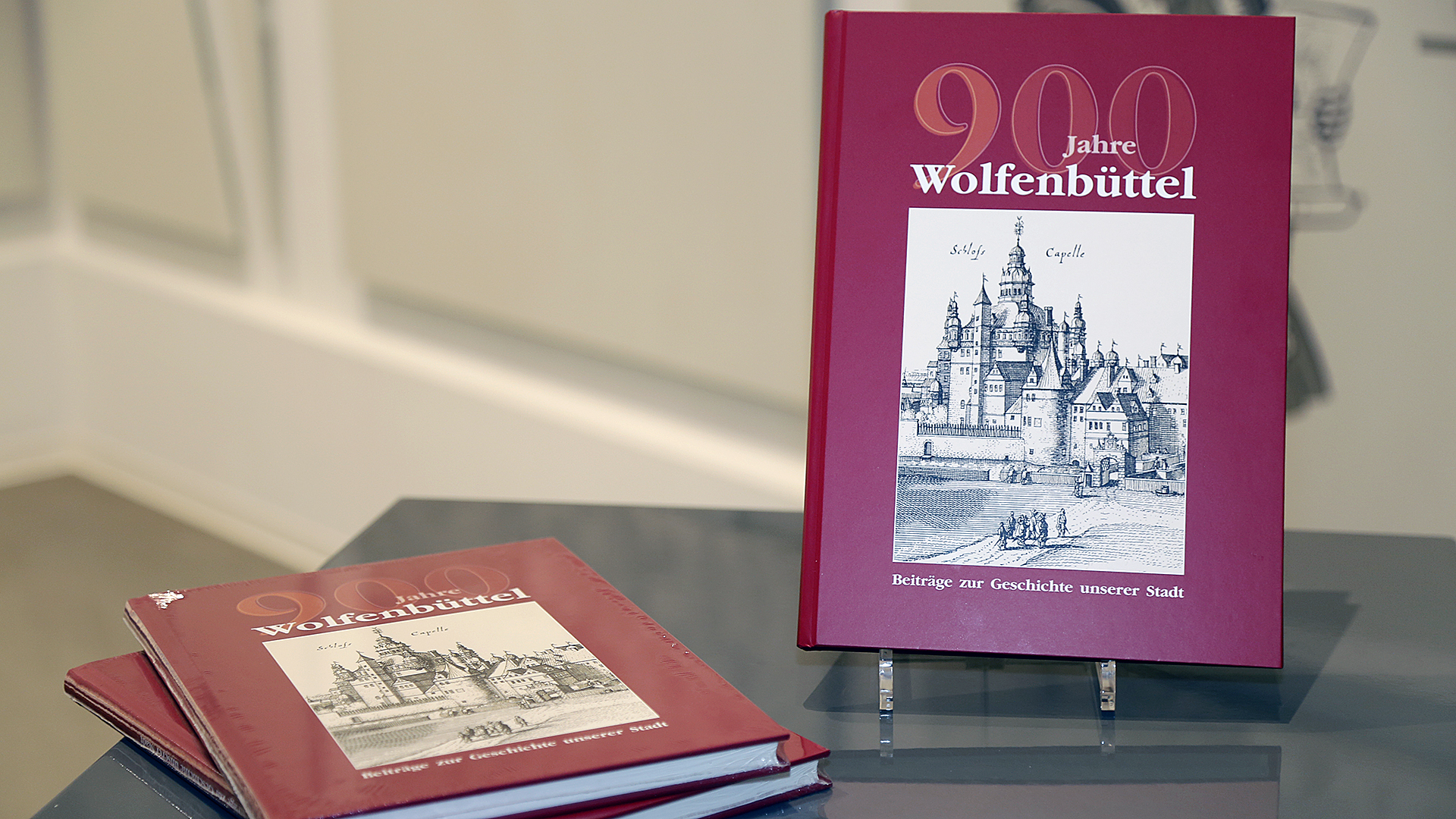 Drei Buchexemplare mit dem Titel "900 Jahre Wolfenbüttel". Während zwei Exemplare auf einem Beistelltisch liegen, steht eines auf einer Buchstütze daneben.