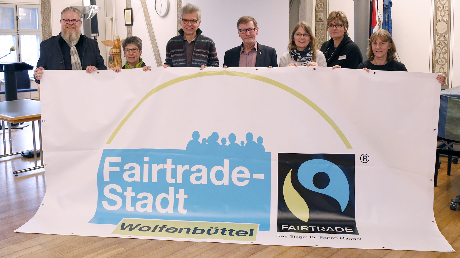 Gruppenfoto von drei Männern und vier Frauen, die auf Banner mit dem Aufdruck "Fairtrade-Stadt Wolfenbüttel" halten.