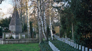 Friedhof mit einzelnen gleichaussehenden Grabsteinen auf einer Rasenfläche. Die Gräber sind mit Efeu bewachsen.