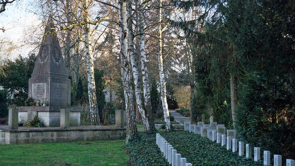 Friedhof mit einzelnen gleichaussehenden Grabsteinen auf einer Rasenfläche. Die Gräber sind mit Efeu bewachsen.