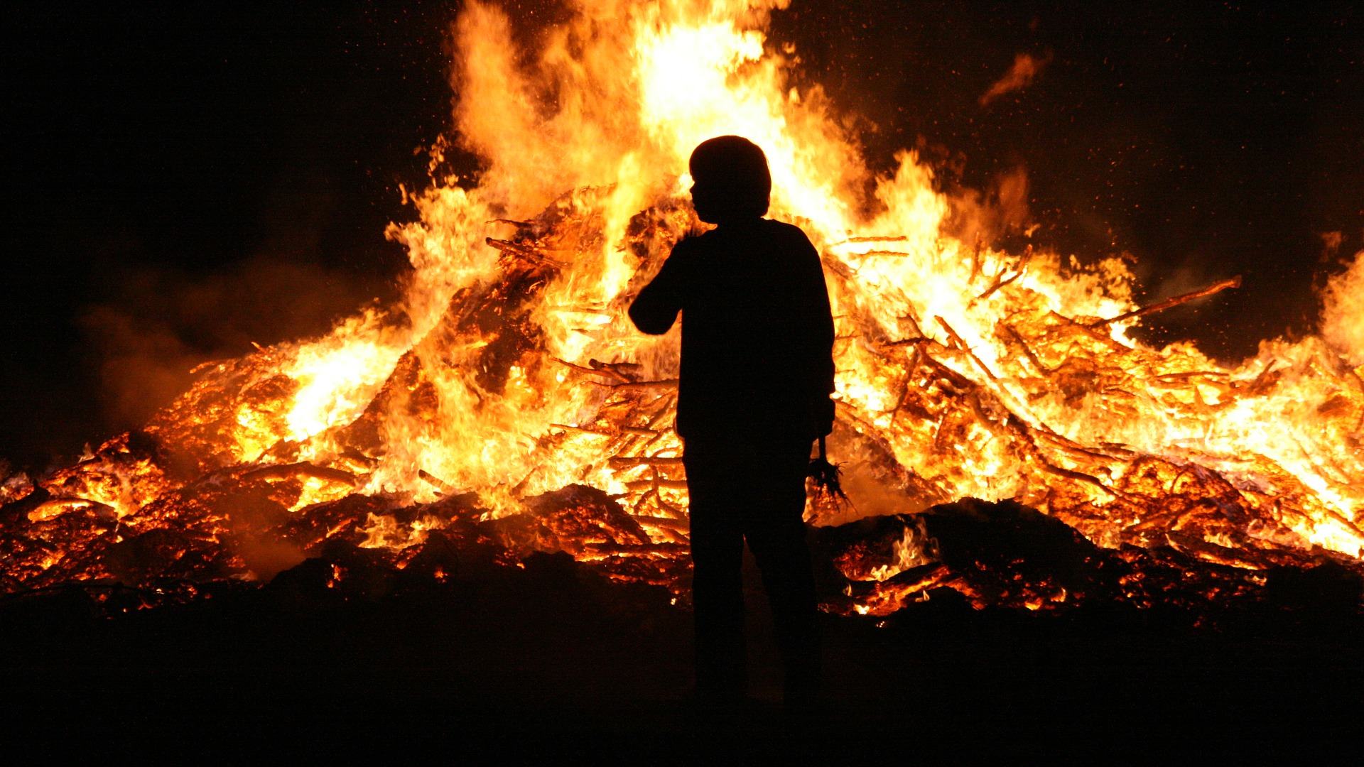 Umriss einer Person, die vor einem hohen Feuer steht.