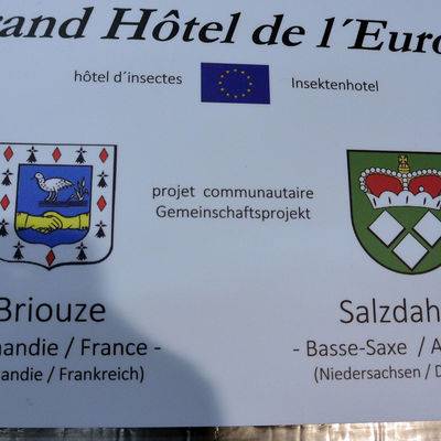 Ein Schild auf dem die Wappen der beiden Partnerstädte Briouze und Wolfenbüttel-Salzdahlum abgebildet sind.