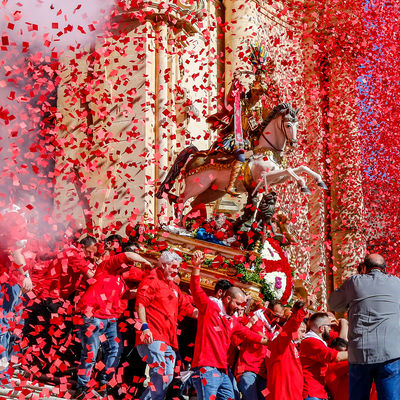 Aus einer Kirche wird eine Reiterstatue getragen. Rotes Konfetti weht in der Luft.
