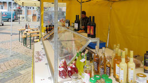 Hinter einem Verkaufsstand auf dem Wolfenbütteler Wochenmarkt steht ein Mann. Auf Tischen und in der Auslage stehen verschiedene Flaschen Wein, Essig und Öle. Auch weitere Lebensmittel sind zu erkennen.