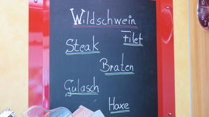 Auf einer Kreidetafel steht "Wildschwein. Filet. Steak. Braten. Gulasch. Haxe."