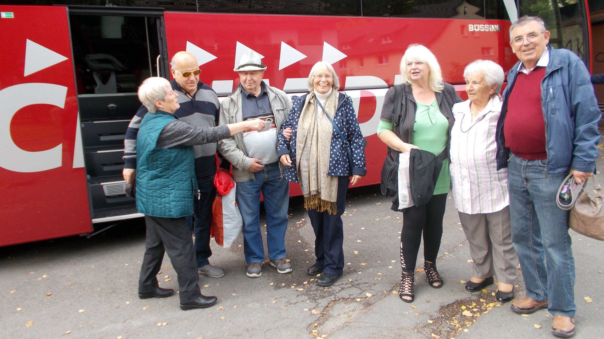 Gruppenfoto von vier Frauen und drei Männern vor einem roten Reisebus.