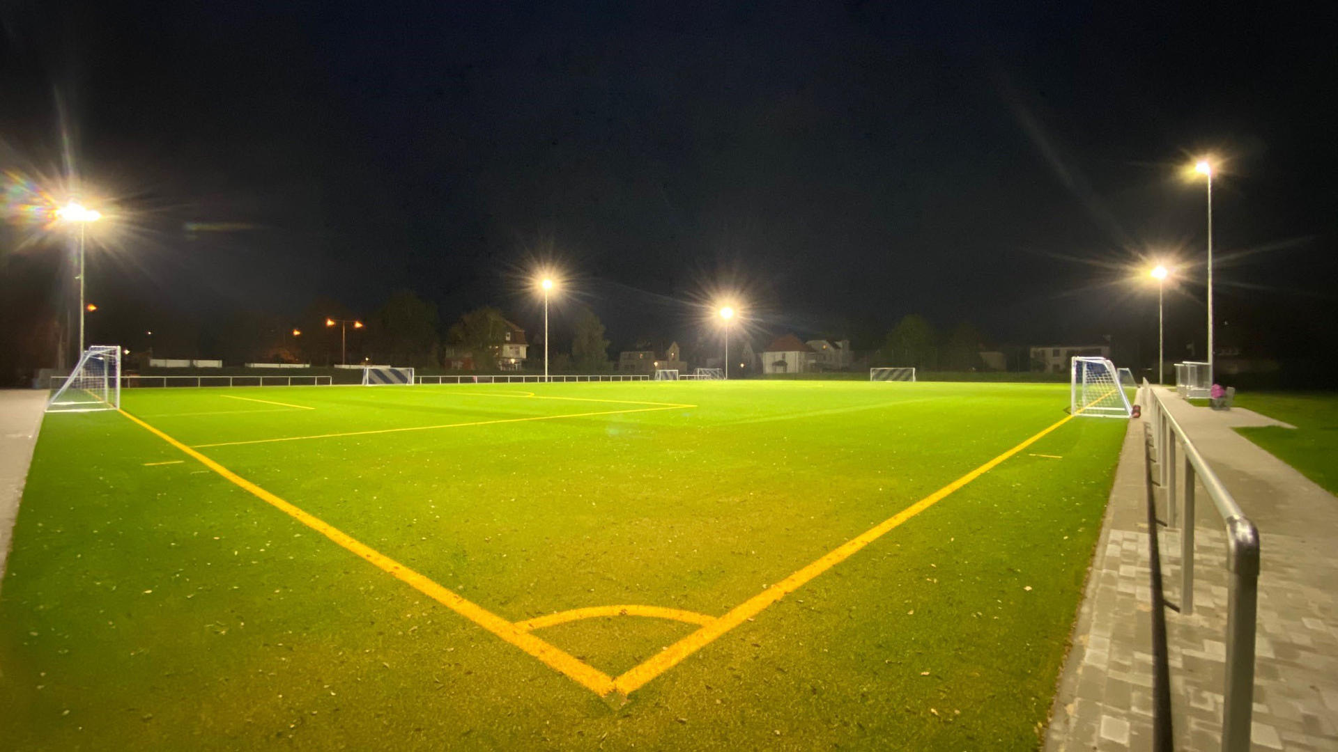 Ein mit Flutlicht ausgeleuchteter Sportplatz mit Seitenlinien und Fußballtoren.