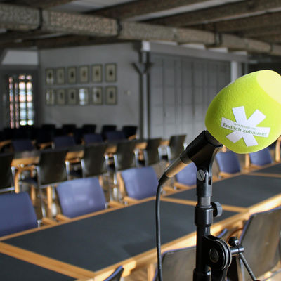 Im Wolfenbütteler Ratssaal stehen Tische und Stühle. Im Vordergrund ist ein Mikrofon mit grünem Popschutz auf einem Mikrofonständer zu sehen.
