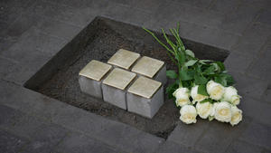 Fünf Stolpersteine sind in eine vorbereitete Öffnung im Pflaster gelegt. Darüber liegt ein Strauß weiße Rosen.