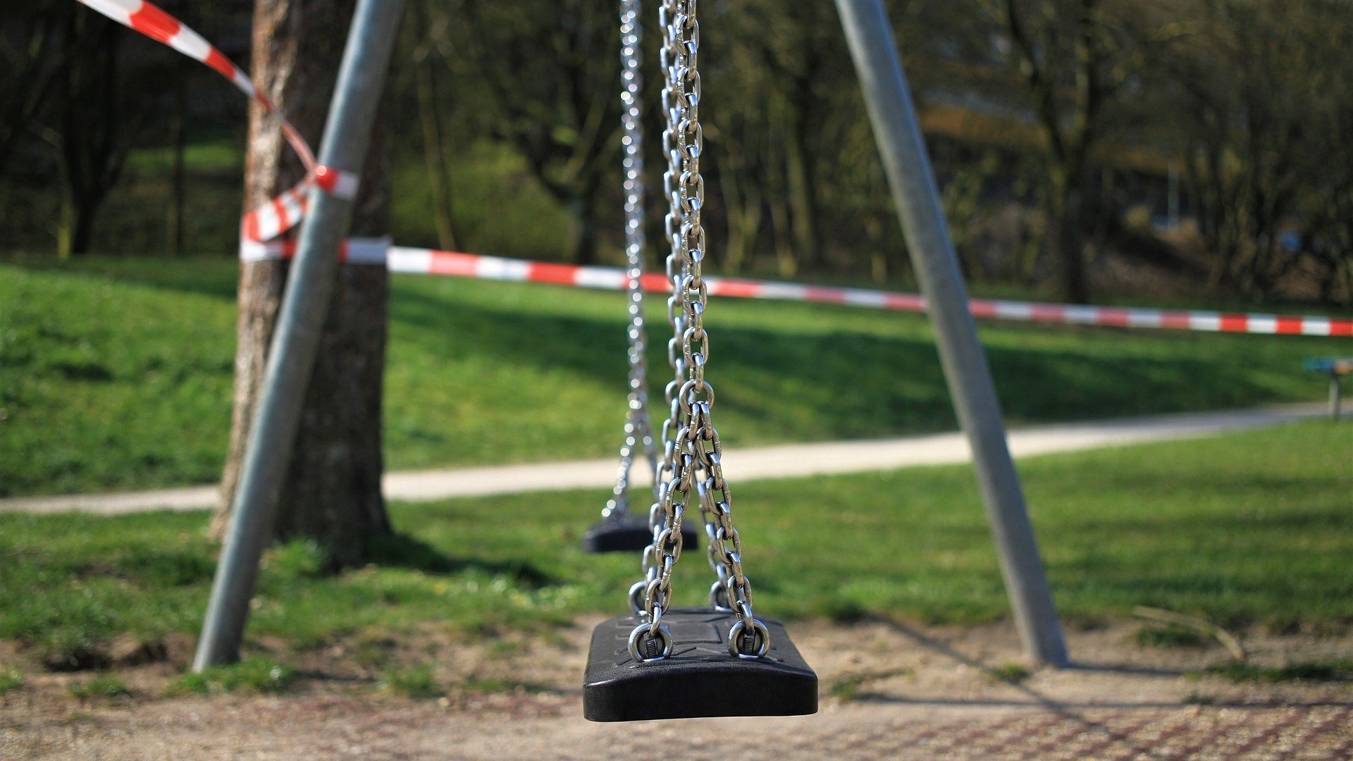 Eine Doppelschaukel auf einem Spielplatz mit rotweißem Flatterband abgesperrt und darf nicht benutzt werden.