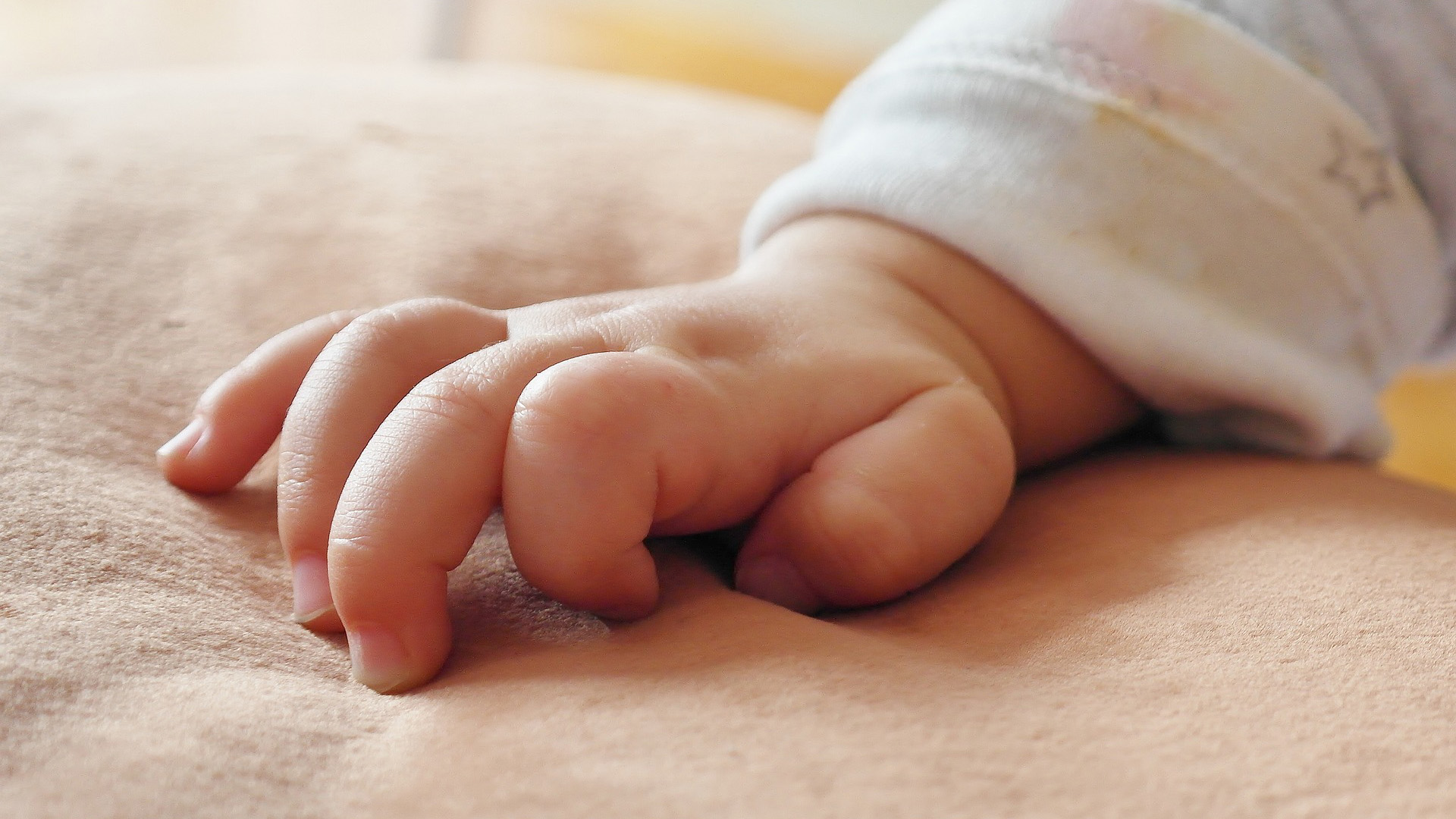 Man sieht die Hand eines Babys mit leicht gekrümmten Fingern auf einer Decke liegen.