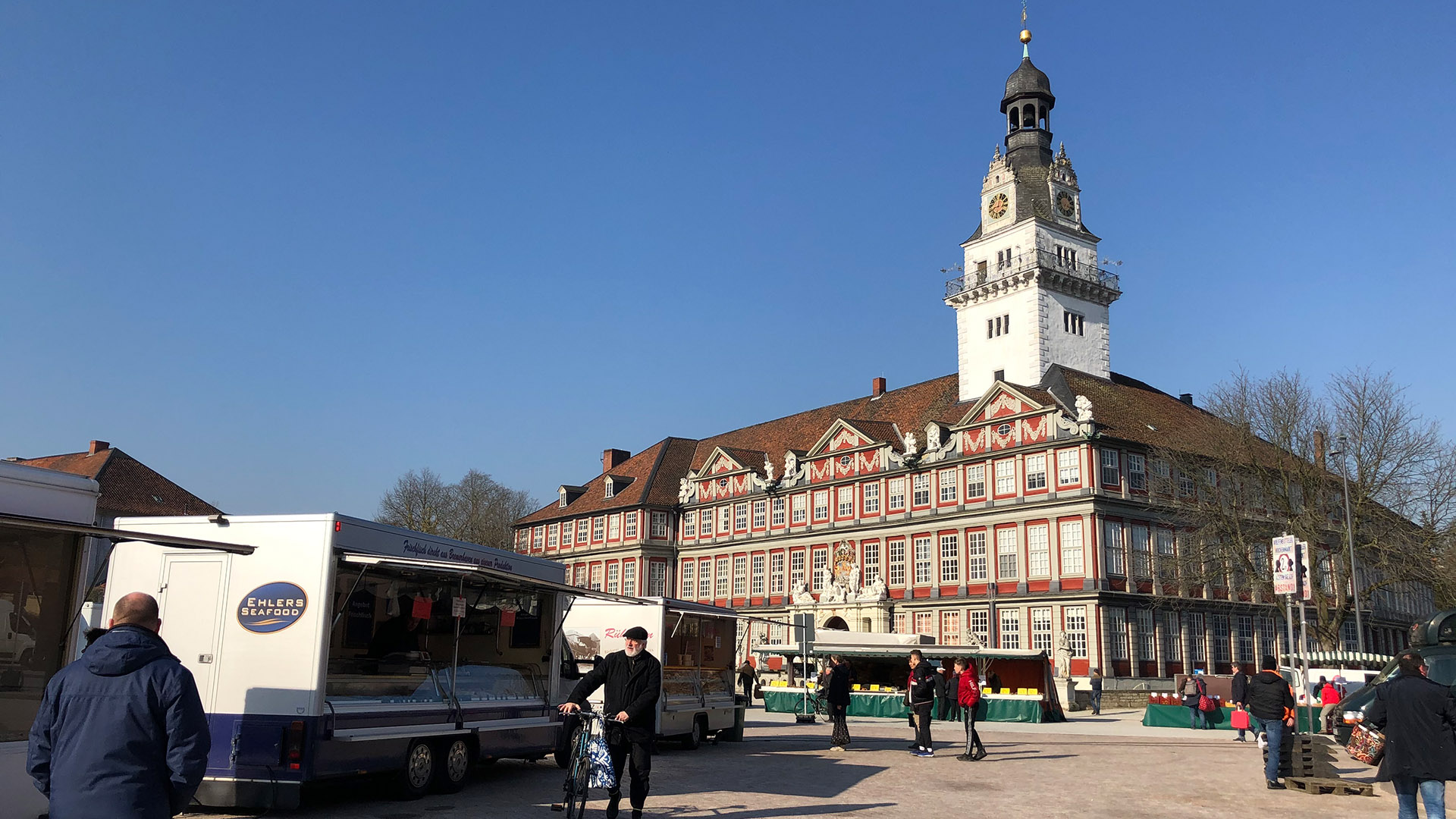 Vor dem Wolfenbütteler Schloss ist der Wochenmarkt aufgebaut. Mit großem Abstand (wegen Covid-19) sind rechts und links Marktstände aufgebaut, Kunden bewegen sich in den breiten Gängen dazwischen.