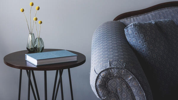 Ausschnitt eines blau-grau gemusterten Sessels vor einer grauen Wand. mit Beistelltisch. Link zur Integrationsseite - Wohnraum gesucht