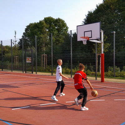 Auf einem Basketballplatz spieln zwei Kinder Basketball.