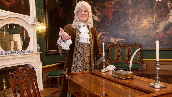 Das Foto zeigt den herzoglichen Tanzmeister im historischen Kostüm neben einem Tisch im Empfangsraum des Wolfenbütteler Schlosses.