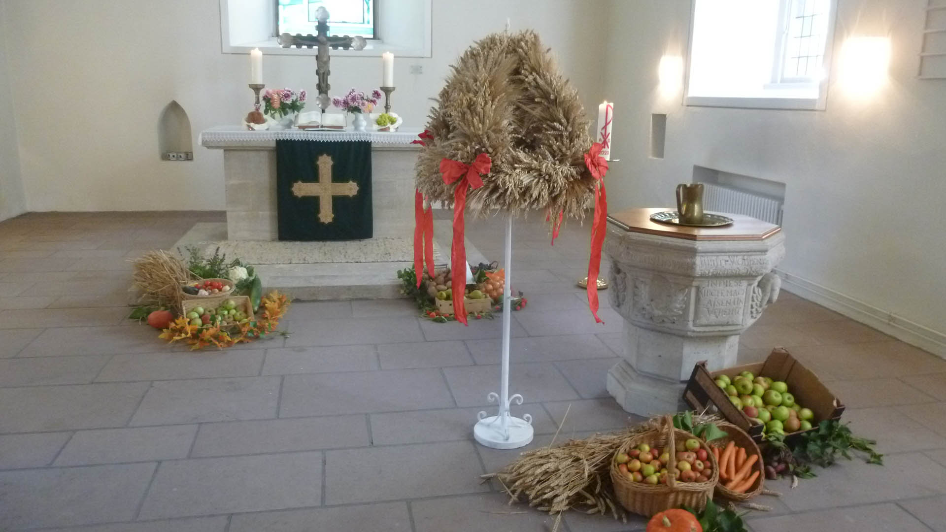 Im Altarraum der Kirche stehen eine Erntekrone und Körbe und Kisten mit Äpfeln, Möhren und anderem Gemüse als Erntedank-Gaben.