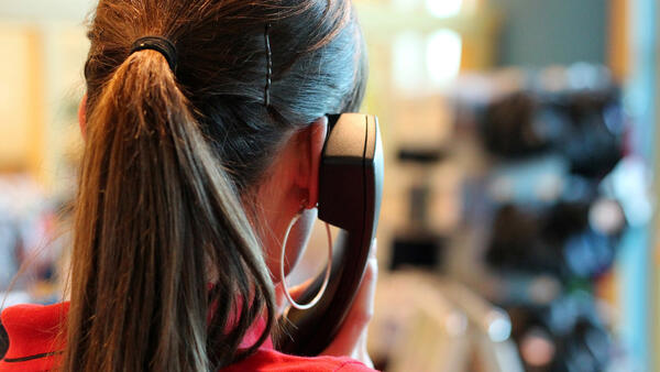 Rückenansicht einer jungen Frau, die sich einen Telefonhörer ans Ohr hält.