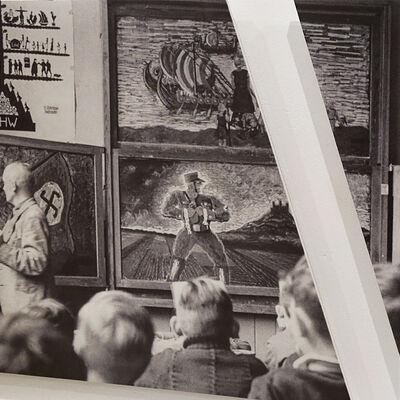 Zu sehen ist eine große Wandplatte. Das aufgedruckte Bild zeigt einen Lehrer in Uniform in der Zeit des Nationalsozialismus