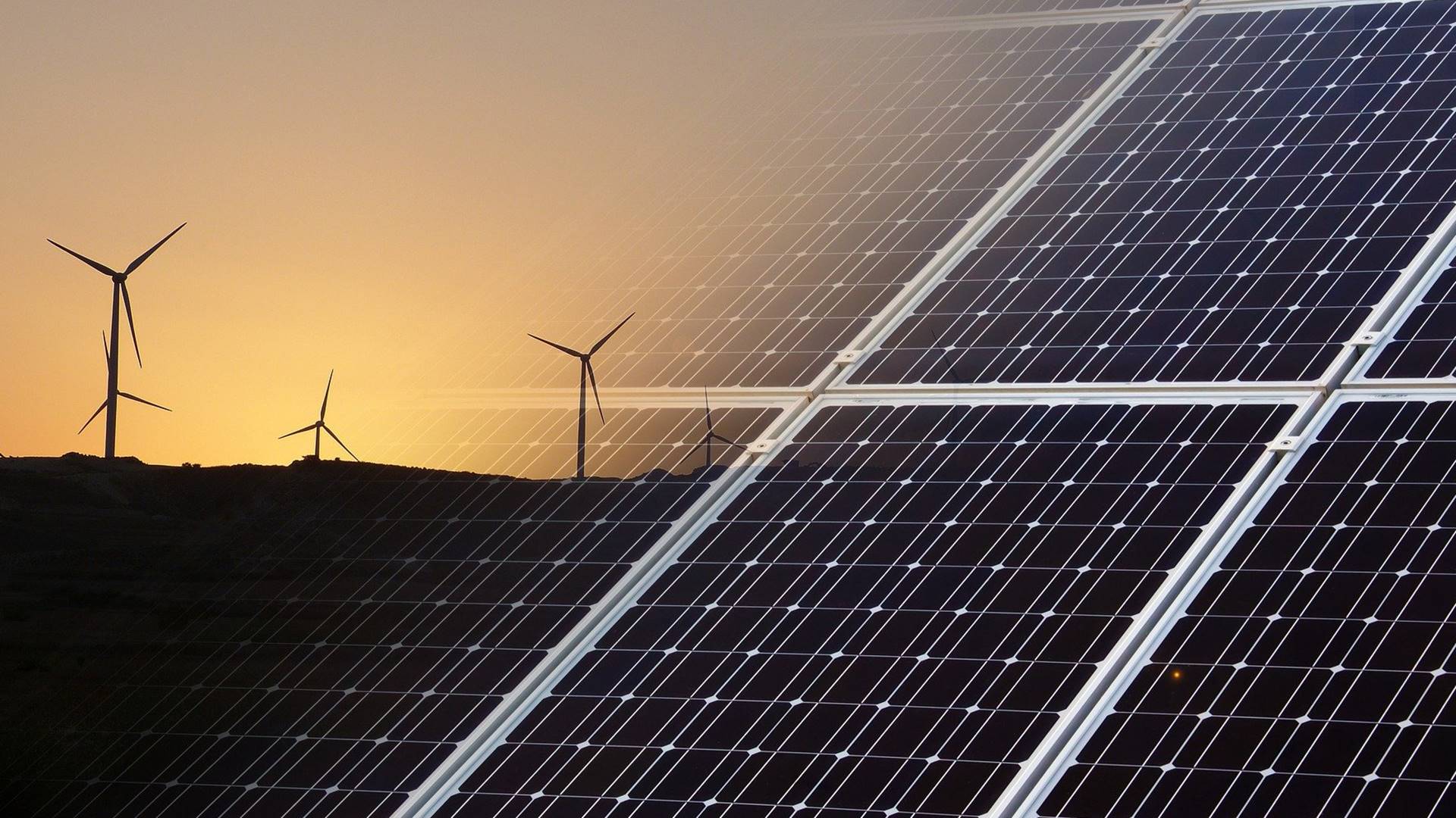 Eine Photovoltaik-Anlage, montiert vor einen Blick auf Windräder bei Sonnenuntergang