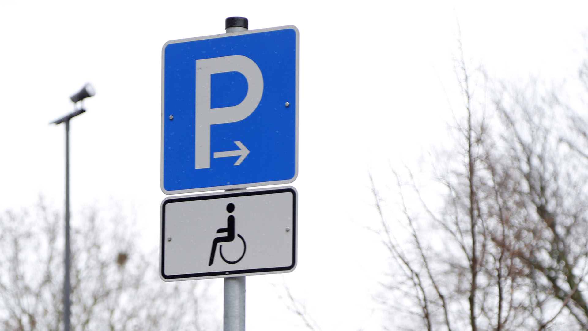 Verkehsschild: ein blaues Schild mit weißem P, darunter ein weiteres Schild mit dem Rollstuhl-Symbol.