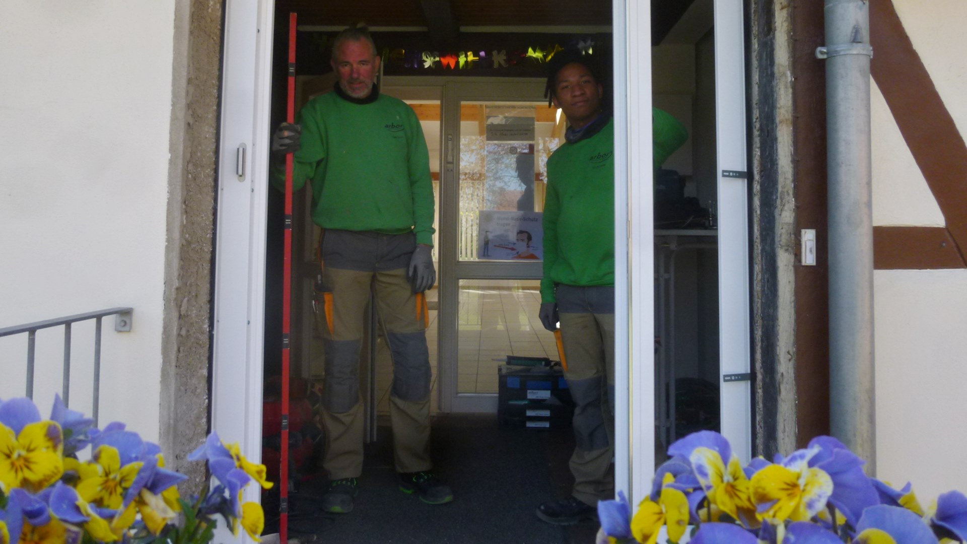 Zwei Handwerker in grünen Pullovern bauen eine Haustür ein.